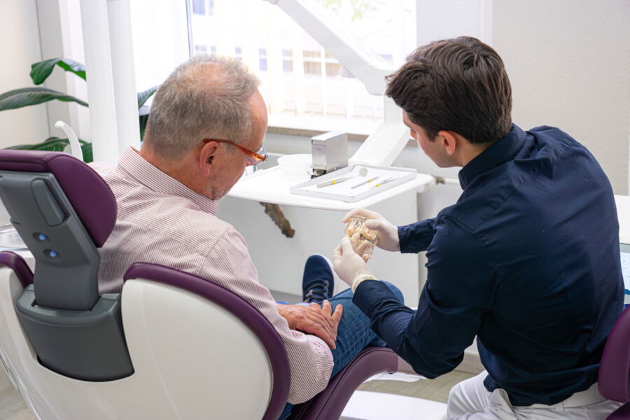 Patient im Zahnarztstuhl wird vom Zahnarzt über bevorstehende Behandlung aufgeklärt